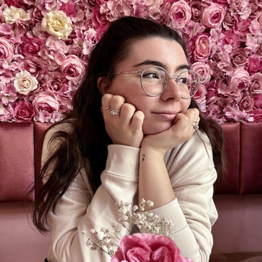 portrait of martina corradini in front of a wall of pink flowers, looking to the right side
